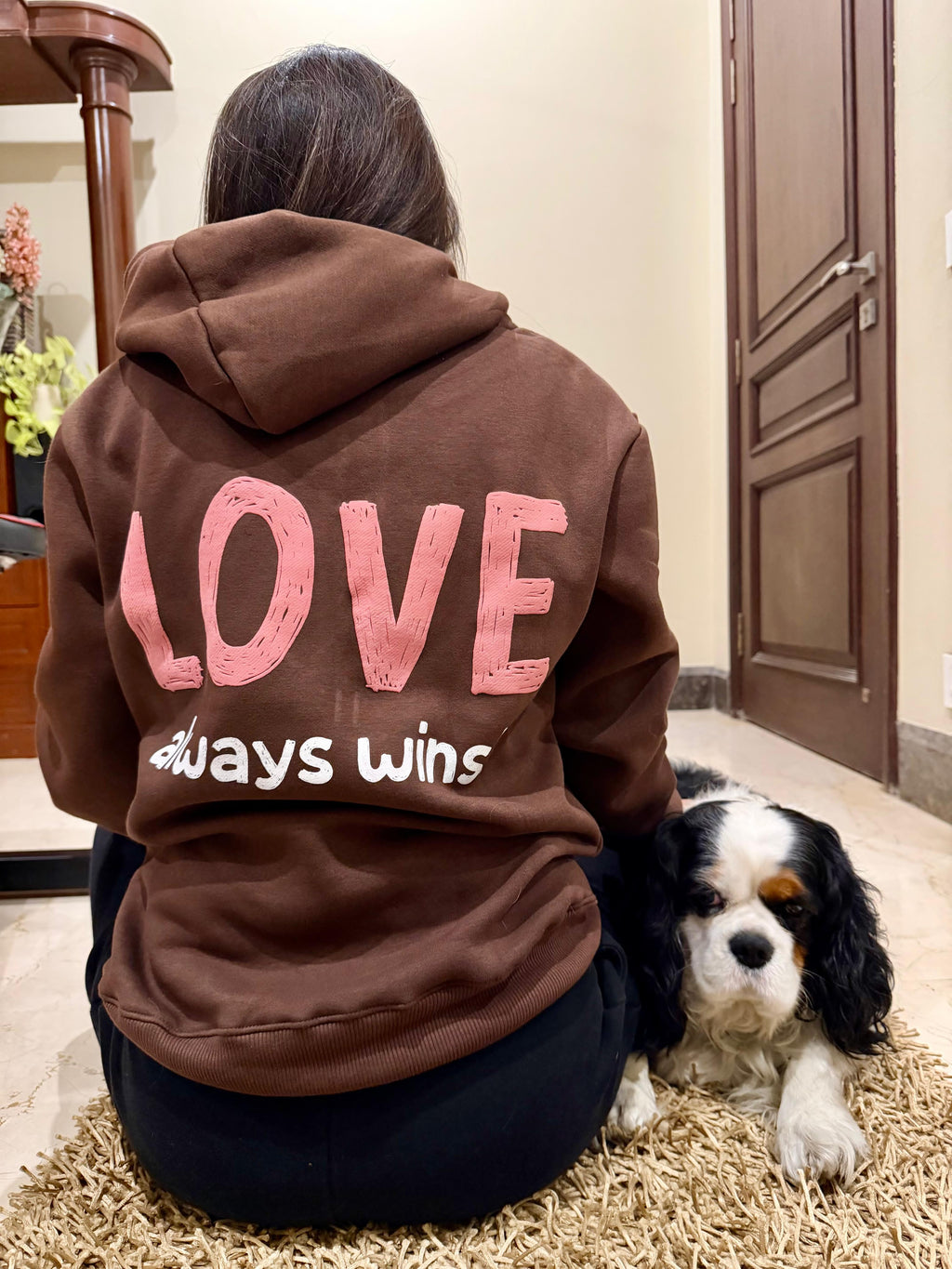 Person wearing a hoodie with 'LOVE always wins' text, sitting on the floor with a dog.